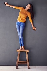 Image showing Portrait, smile and chair with woman in studio for fashion, casual and confident style. Happiness, trendy and funny with young female person laughing on gray background for mockup space and joy