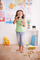 Image showing Kid, toy and blowing bubbles for childhood development, playing and having fun alone in room. Happy, growth and face of young girl in kindergarten for learning, soap bubble wand and activity games