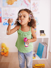 Image showing Girl, toy and blowing bubbles for development, playing and having fun alone in room. Happiness, growth and face of young child in kindergarten for learning, soap bubble wand and activity games
