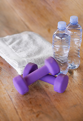 Image showing Closeup, water bottles and towel with dumbbells, ground and exercise with equipment and nutrition. Weights, h2o and cloth with wooden floor or fitness with workout or training with wellness or health