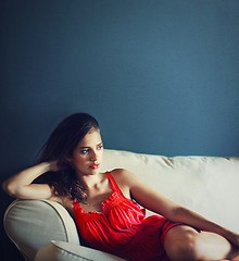 Image showing Relax, sexy and space with woman on sofa in studio on blue background for feminine wellness. Beauty, fashion and thinking with confident or serious young person in red dress for valentines day