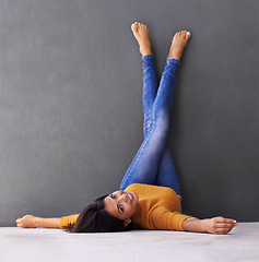 Image showing Portrait, woman and smile to relax on floor with a dark wall background in casual style. Leisure, rest and face of female person with rest and fashion upside down with her feet on a studio backdrop