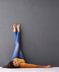 Image showing Portrait, floor and happy woman relax with casual style on a grey wall background for rest. Leisure, style and face of smiling female person upside down on a dark studio backdrop for fashion