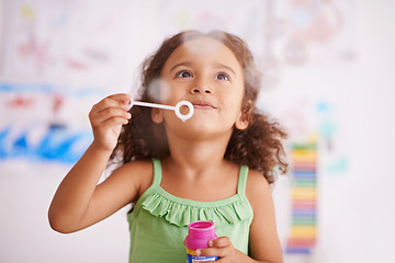 Image showing Child, toy and blowing bubbles for development, playing and having fun alone in home. Happiness, bokeh and face of young girl in bedroom for entertainment, soap bubble wand and activity games