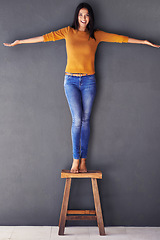 Image showing Woman, confident and stand on chair in portrait, smile and fashion on wall background. Female person, clothes and happy lady on stool, apparel and trends in living room at home in house