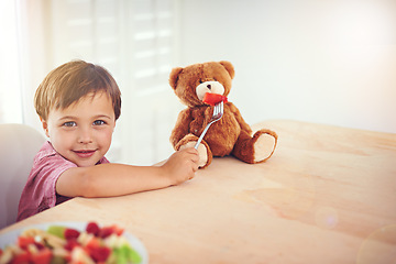 Image showing Child, portrait and feeding fruit to teddy bear with fantasy play, imagination and watermelon for nutrition in dining room. Boy, kid and stuffed animal with breakfast bowl at lounge table for sharing