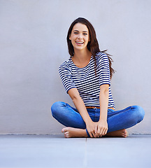 Image showing Portrait, legs crossed and woman on the floor, fashion and cheerful girl on a grey background. Person, wall and model on the ground and casual outfit with confidence and proud with peace and funny