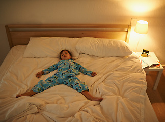 Image showing Boy, bed and rest for night, sleeping and tired with fatigue and peace. Child, dreaming and exhausted with pyjamas, dark and bedroom with lamp for serene childhood at home or house for calm kid