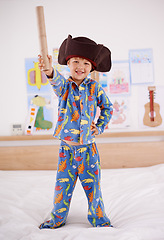 Image showing Child, portrait and happy for pirate game, character and creativity in bedroom or at home. An excited boy or kid on a bed with cardboard, cap and pajamas for fun holiday, imagination and play alone