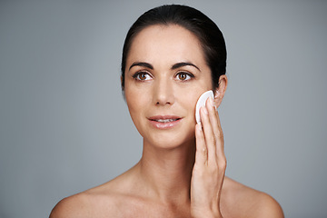 Image showing Mature woman, pad and clean in studio, skin care and facial treatment on gray background. Female person, cotton and swab for grooming in daily routine, mockup space and dermatology to remove makeup