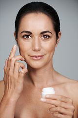 Image showing Portrait, woman and apply cream for skincare in studio isolated on a gray background. Face, cosmetics and mature model with moisturizer in container for dermatology, beauty or hydration for antiaging