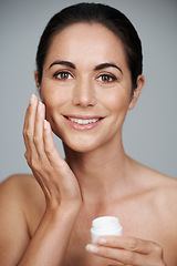 Image showing Portrait, happy woman and apply cream for skincare in studio isolated on a gray background. Face, cosmetics and mature model with moisturizer in jar for dermatology, beauty or hydration for antiaging