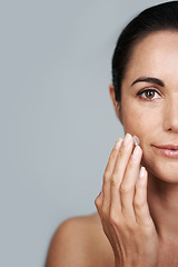 Image showing Portrait, beauty and lotion with mature woman in studio on gray background for hydration or wellness. Half face, skincare or cream and serious model with moisturizer in hand to apply for antiaging