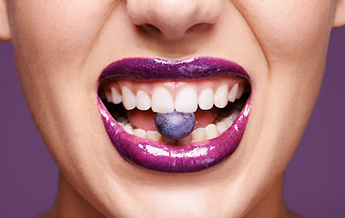 Image showing Beauty, lipstick and woman with blueberry in mouth, organic makeup and creativity with shiny cosmetic product. Vegan, eco friendly and purple lip gloss for aesthetic with fruit on studio background