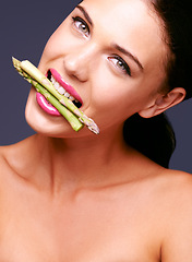 Image showing Woman, lipstick and vegetables in mouth in portrait, beauty and nutrition for vegan cosmetic product in studio. Cruelty free makeup, cosmetology and asparagus with pink lip gloss on grey background