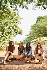 Image showing Friends, road and girl with skateboard in smile at forest for hobby in outdoor and activity in California. Diverse group, teen and sit for happiness on school holiday or break and together in woods