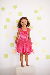 Image showing Child, girl and smile with standing against wall with sticky notes, ottoman and excited with creativity. Kid, female person and happy with playing for development, growth and cute in pink dress