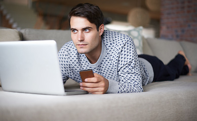 Image showing Man, laptop and smartphone at home on sofa for remote work as freelance, journalist and online research for newspaper. Male person, living room and focus on internet with information for article.