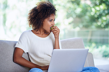 Image showing Laptop, apple and African woman eating, sofa and afro while at home lounge for relax. Technology, computer or scrolling on social media website, app or internet for connection and with healthy snack
