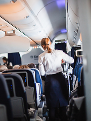 Image showing Interior of airplane with passengers on seats and stewardess in uniform walking the aisle, serving people. Commercial economy flight service concept.