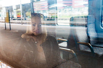 Image showing Woman traveler contemplating outdoor view from window of train. Young lady on commute travel to work sitting in bus or train.