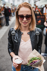 Image showing Beautiful young woman holding delicious organic salmon vegetarian burger and homebrewed IPA beer on open air beer an burger urban street food festival in Ljubljana, Slovenia.