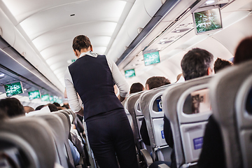 Image showing Interior of airplane with passengers on seats and stewardess in uniform walking the aisle, serving people. Commercial economy flight service concept.