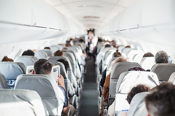 Image showing Interior of airplane with passengers on seats and stewardess in uniform walking the aisle, serving people. Commercial economy flight service concept.