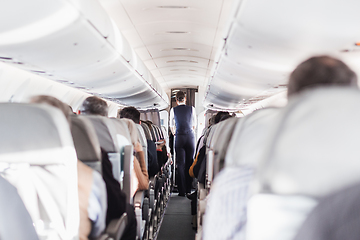 Image showing Interior of airplane with passengers on seats and stewardess in uniform walking the aisle, serving people. Commercial economy flight service concept.