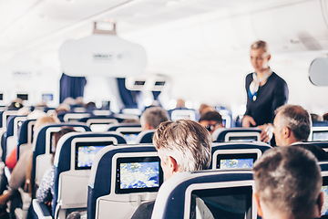 Image showing Interior of airplane with passengers on seats and stewardess in uniform walking the aisle, serving people. Commercial economy flight service concept.