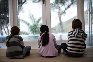 Image showing Rain, window and sad child on a floor unhappy, upset or annoyed by bad weather at home. Glass, disappointed and sibling kids in a living room frustrated by storm, cold or unexpected winter disaster