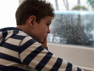 Image showing Window, rain and sad boy child on a floor unhappy, upset or annoyed by bad weather in his home. Glass, depression and kid in a living room frustrated by storm, cold or unexpected winter disaster