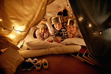 Image showing Portrait, children and siblings with pot helmet in a fort for fantasy, learning or playing in their home. Happy family, face and kids on a floor with tent games, development or learning in a house