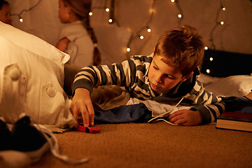 Image showing Toy, car and boy child playing on a floor at night in a house for fun, learning or sibling sleepover. Riding, games and kid with racecar in a living room for driving, fantasy or dream with family