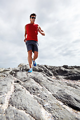 Image showing Male runner, rocky terrain and training, exercising outdoors and seaside for marathon. Fitness, sports and sunglasses for active endurance athlete, health and cardio heart wellness for dedicated man