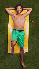 Image showing Happy man, portrait and lying with towel on green grass above for relaxation or outdoor summer holiday. Top view of young male person with smile in relax for swimwear or fashion on field in nature