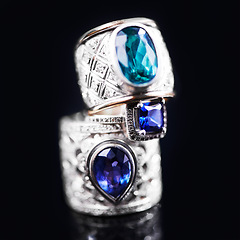 Image showing Gemstone, silver and rings on a black background of luxury or expensive present for engagement or marriage in studio. Jewelry, diamonds and blue or sapphire rock in closeup, stack and rich accessory