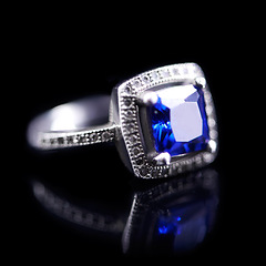 Image showing Blue, silver and ring on a black background for luxury, expensive and present for engagement or marriage in studio. Jewelry, diamonds and crystal rock in closeup with shine and reflection for a gift