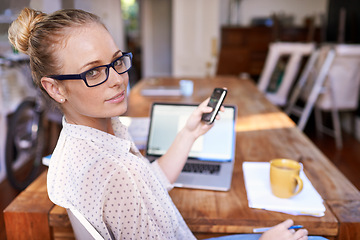 Image showing Woman, phone and laptop on table in home office for remote work, startup and text online with coffee.Young person and smile with tech for internet, research and scroll for message indoor on blurred