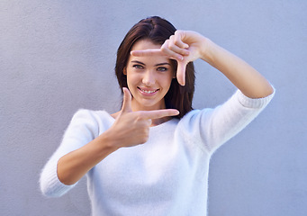 Image showing Portrait, wall and woman with finger frame, smile and focus for creative fashion photography. Perspective, hand gesture and girl showing happy face, casual style and view finder on blue background.