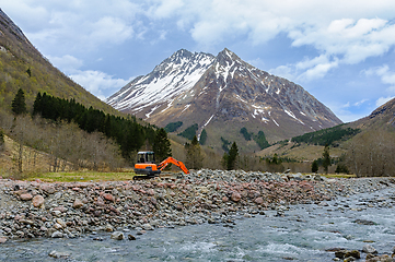 Image showing Majestic mountain backdrop behind an excavator at riverbank duri