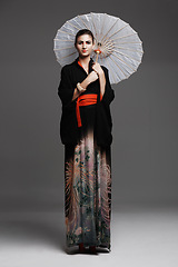 Image showing Portrait, smile and Japanese woman with traditional outfit and confidence on a studio background. Person, stylish clothes and Asian with model and elegant with umbrella and proud with culture or girl