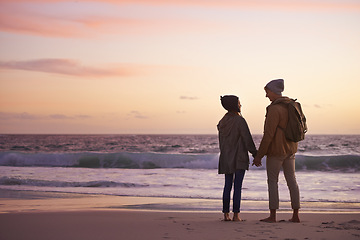 Image showing Couple, holding hands and love at sunset by water, ocean waves and peace for romance in relationship. People, back and security in marriage, sea and travel together on vacation or holiday for date