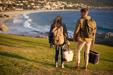 Image showing Love, walking and couple on hike with ocean, sunset for tropical holiday adventure, relax and bonding together. Picnic, man and woman on romantic date on beach, nature and grass on vacation from back