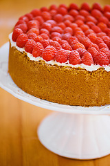 Image showing Stand, frosting and cheesecake with raspberries on table for sweet snack for tea time at home. Bakery, catering and closeup of gourmet dessert with crust, cream and fresh organic fruit in dining room