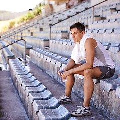 Image showing Stadium, man and athlete to relax in outdoor and commitment to fitness for sprinting competition. Person, competitive and runner with confidence in sport, planning and exercise with water on stands