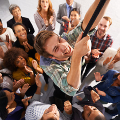 Image showing Business people, smile and man climbing rope for goals, target or achievement with team support. High angle, diversity and happy professional person with group of colleagues for ambition in office.