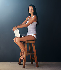 Image showing Laptop, portrait and woman on chair to relax in studio with gray wall background for social media. Computer, smile and underwear with happy young person sitting on stool for blogging or streaming