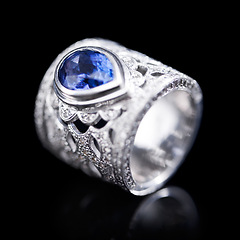 Image showing Gemstone, silver and ring on a black background of luxury or expensive present for engagement or marriage in studio. Jewelry, diamonds and blue or sapphire rock in closeup, reflection and accessory