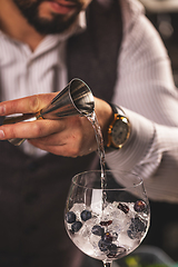Image showing Bartender pouring gin into glass with ice and berries